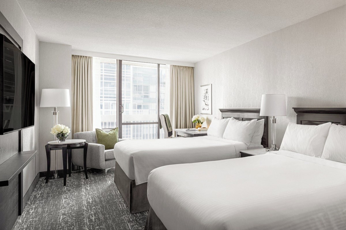 A hotel room with two beds, a desk, a chair, a TV, and a window with curtains.