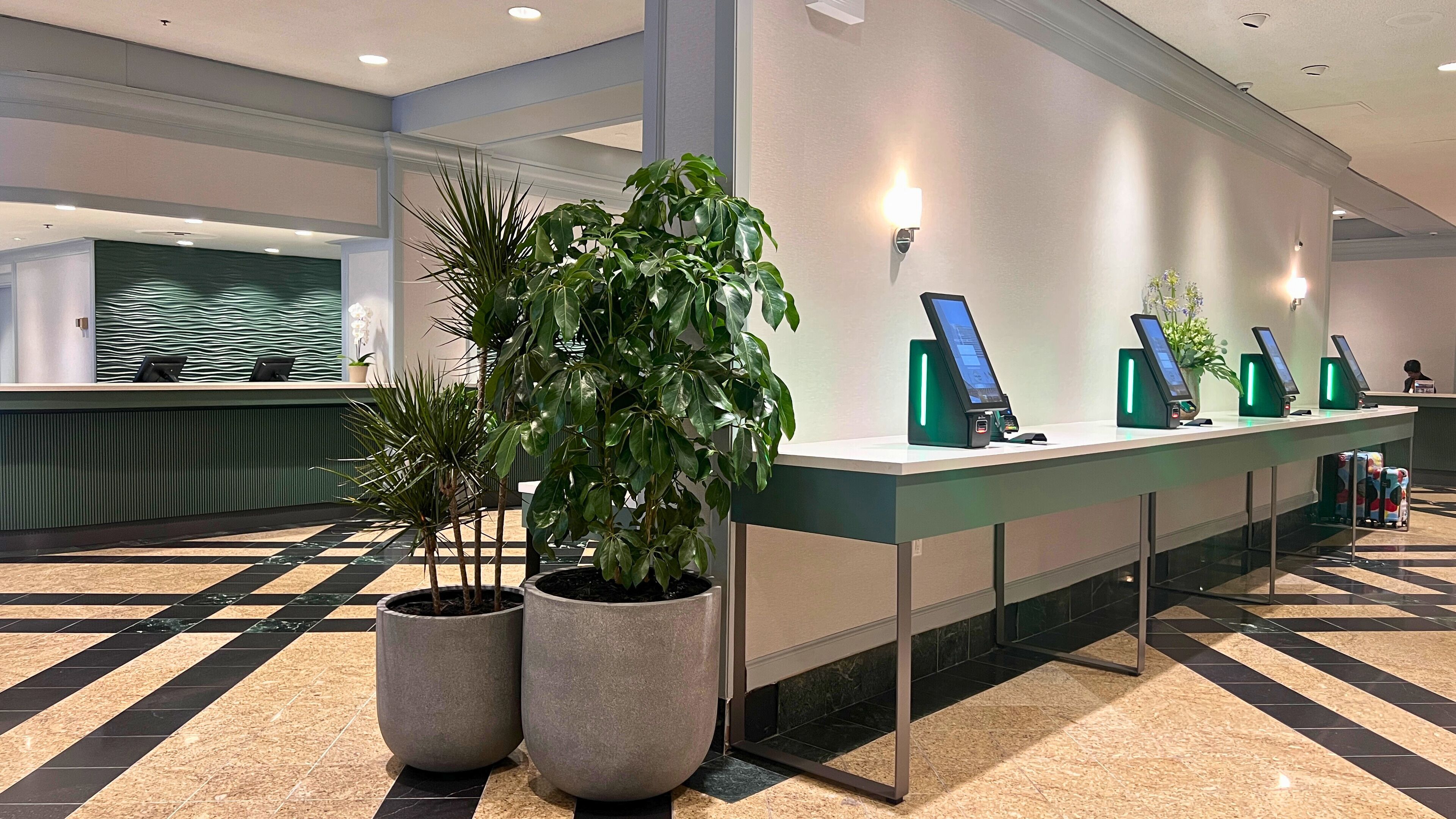 Un área de recepción con mostrador de registro, plantas en macetas y quioscos de autoservicio.