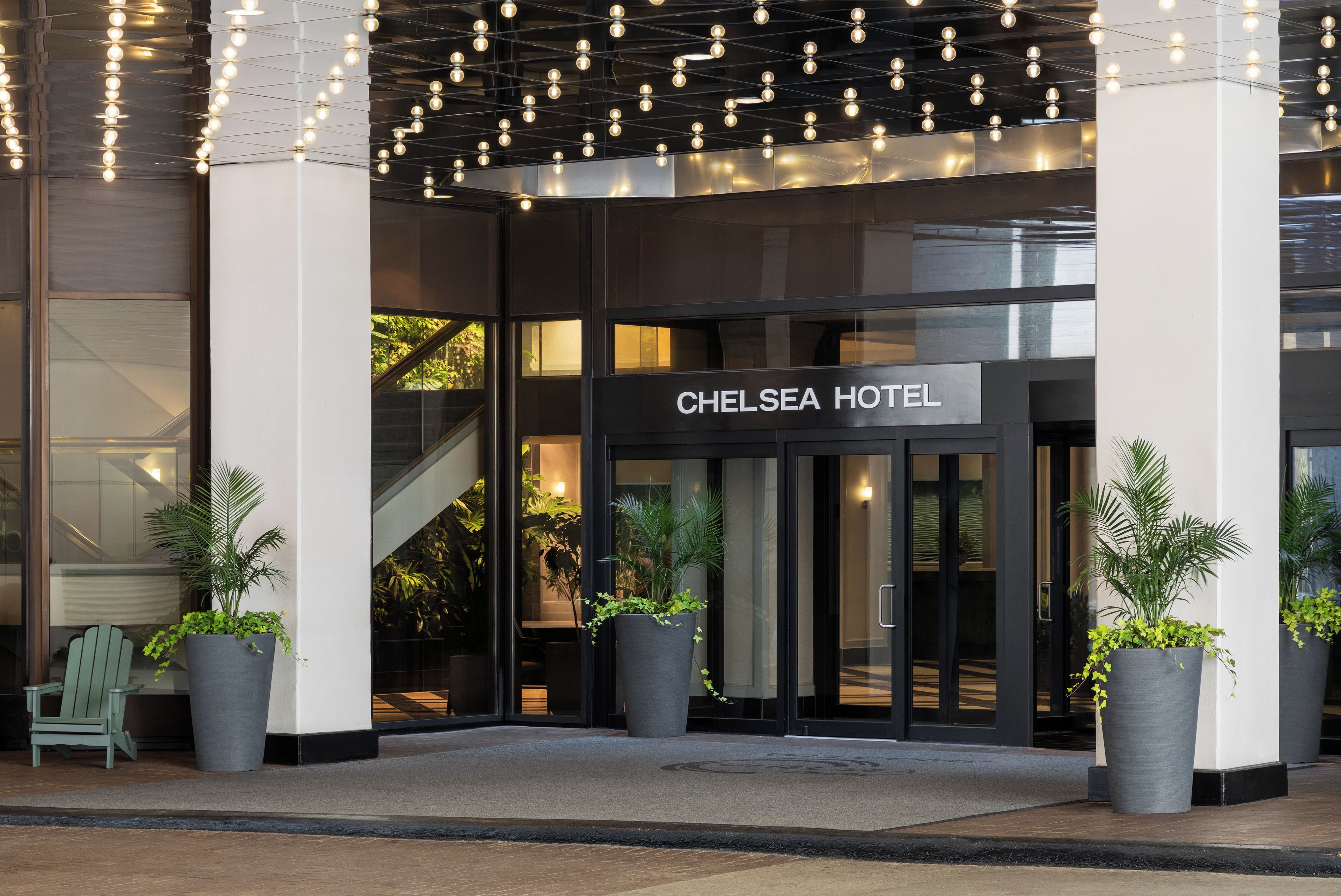 The entrance of the Chelsea Hotel with a sign, potted plants, and a staircase leading to the interior.