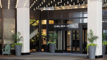 The entrance of the Chelsea Hotel with a sign, potted plants, and a staircase leading to the interior.