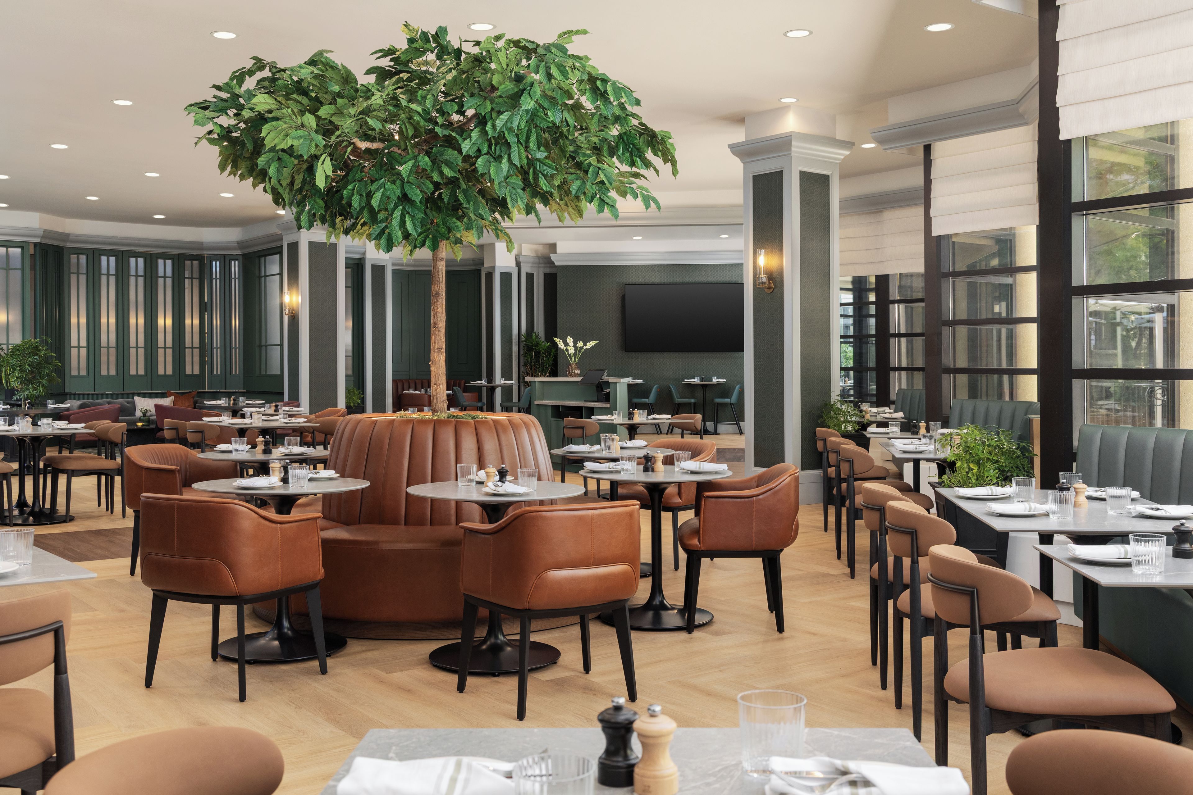 Ein Restaurant mit mehreren Tischen und Sitzgelegenheiten, einem großen Kunstbaum und einem modernen Ambiente.