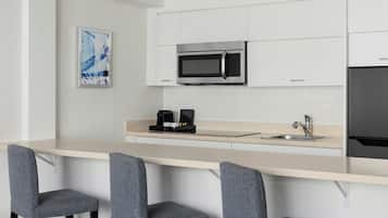 A modern kitchen with white cabinets, a stainless steel microwave, a sink, and two bar stools.