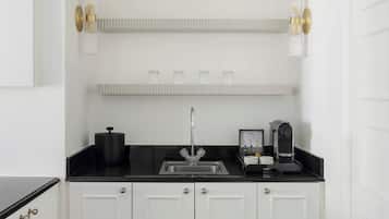 A kitchen with a black countertop, white cabinets, a stainless steel sink, and a coffee machine.