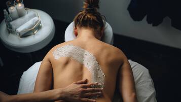 A person receiving a back treatment with a white substance, a candle, and a small table with a geometric container.