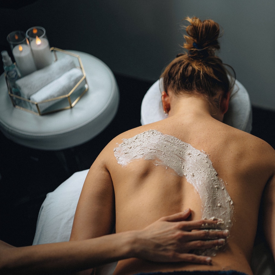 A person receiving a back treatment with a white substance, a candle, and a small table with a geometric container.