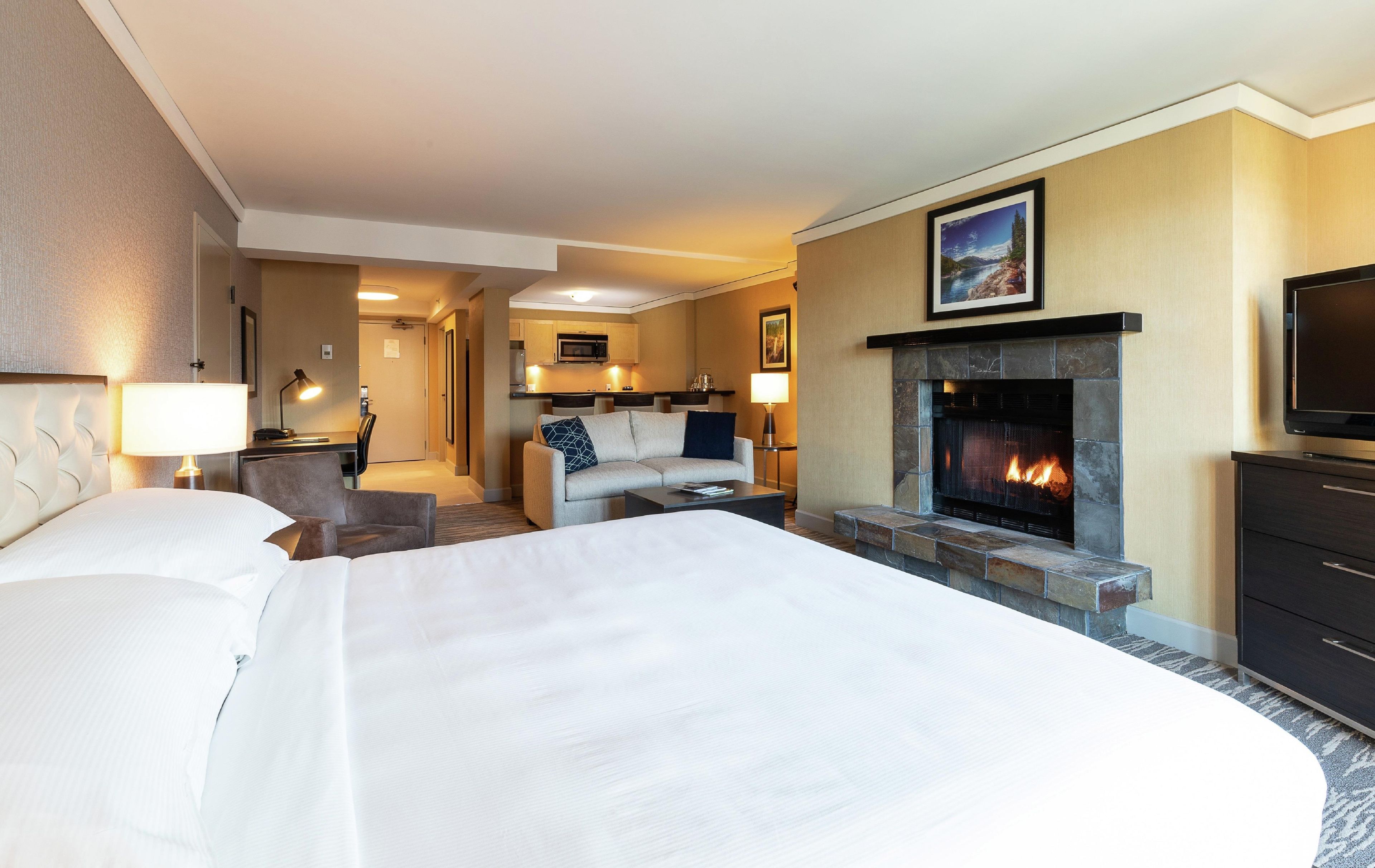 A hotel room with a large bed, a fireplace, a television, and a dining area.
