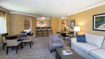 Una habitación de hotel con zona de comedor, sofá, mesa de centro y televisión.