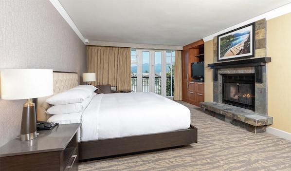 A hotel room with a large bed, a TV, a fireplace, and a view of mountains through the windows.