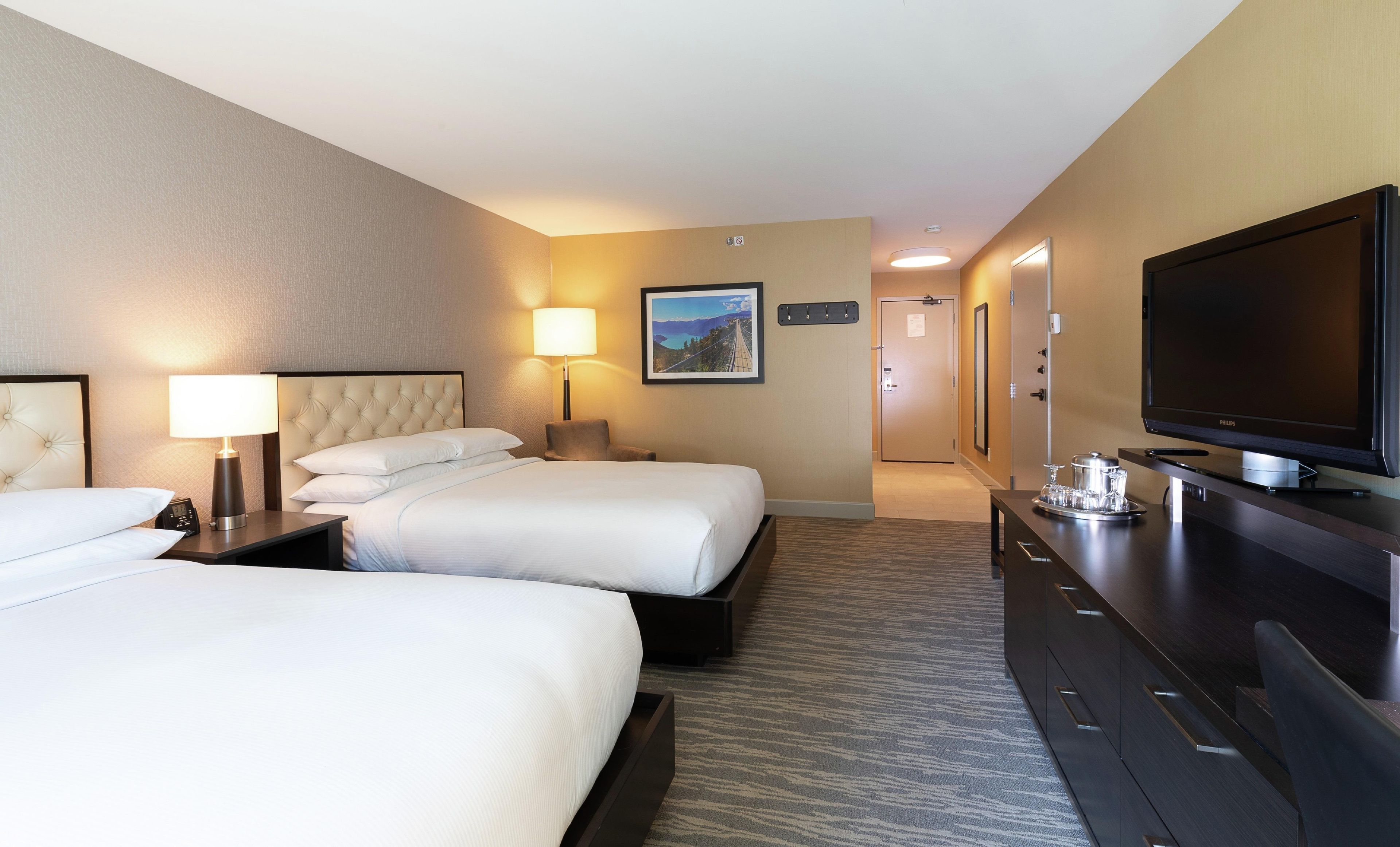 A hotel room with two beds, a television, a desk, and a lamp.