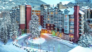 Un hotel de varios pisos con un patio central, rodeado de árboles nevados y montañas al fondo.