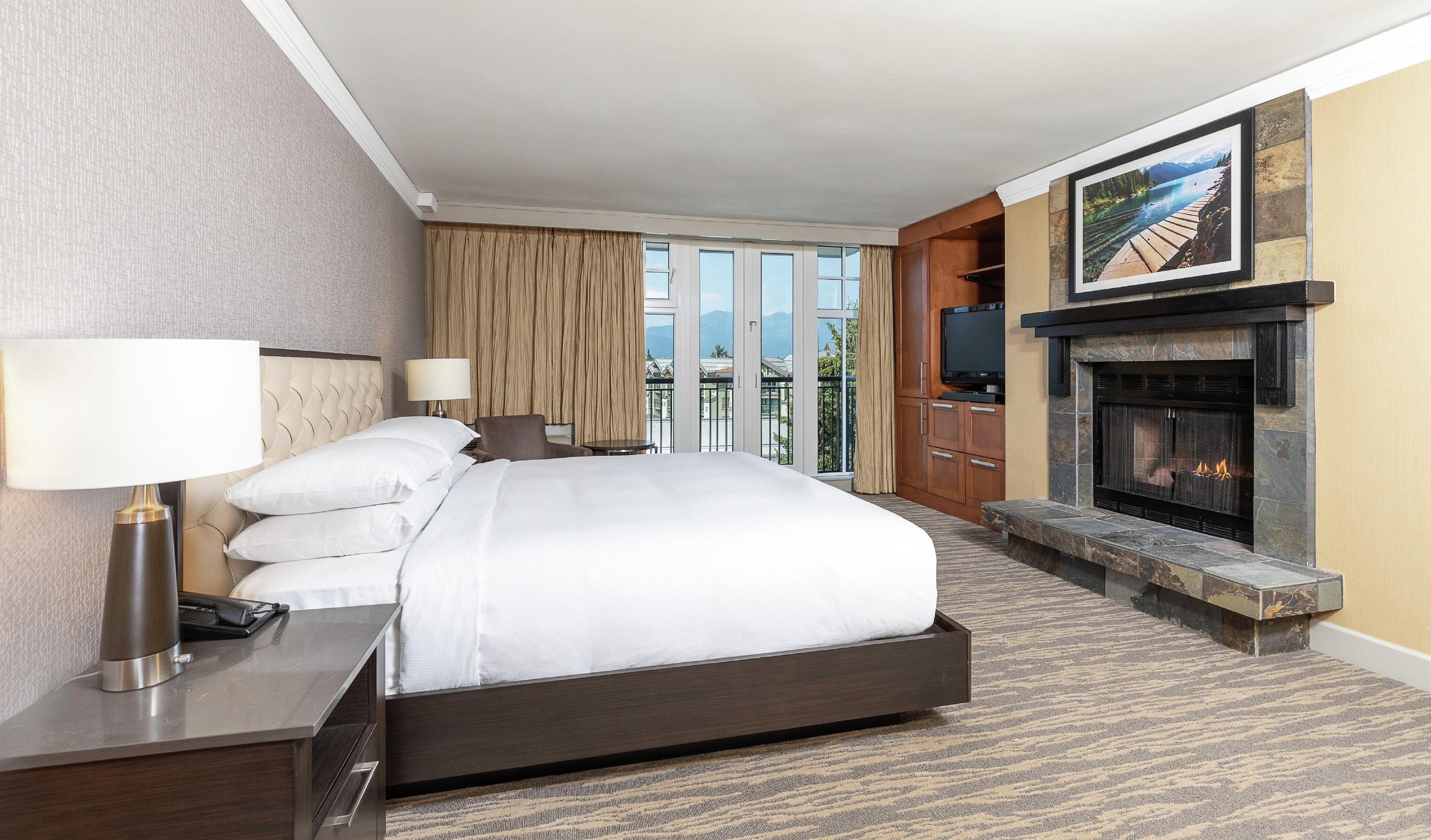 Habitación de hotel con una cama grande, televisión, chimenea y vistas a las montañas a través de las ventanas.