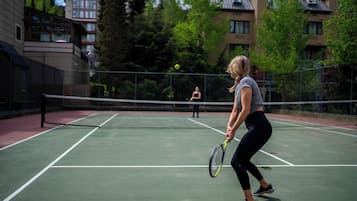 Una cancha de tenis al aire libre con una red en el centro, rodeada de edificios y árboles.