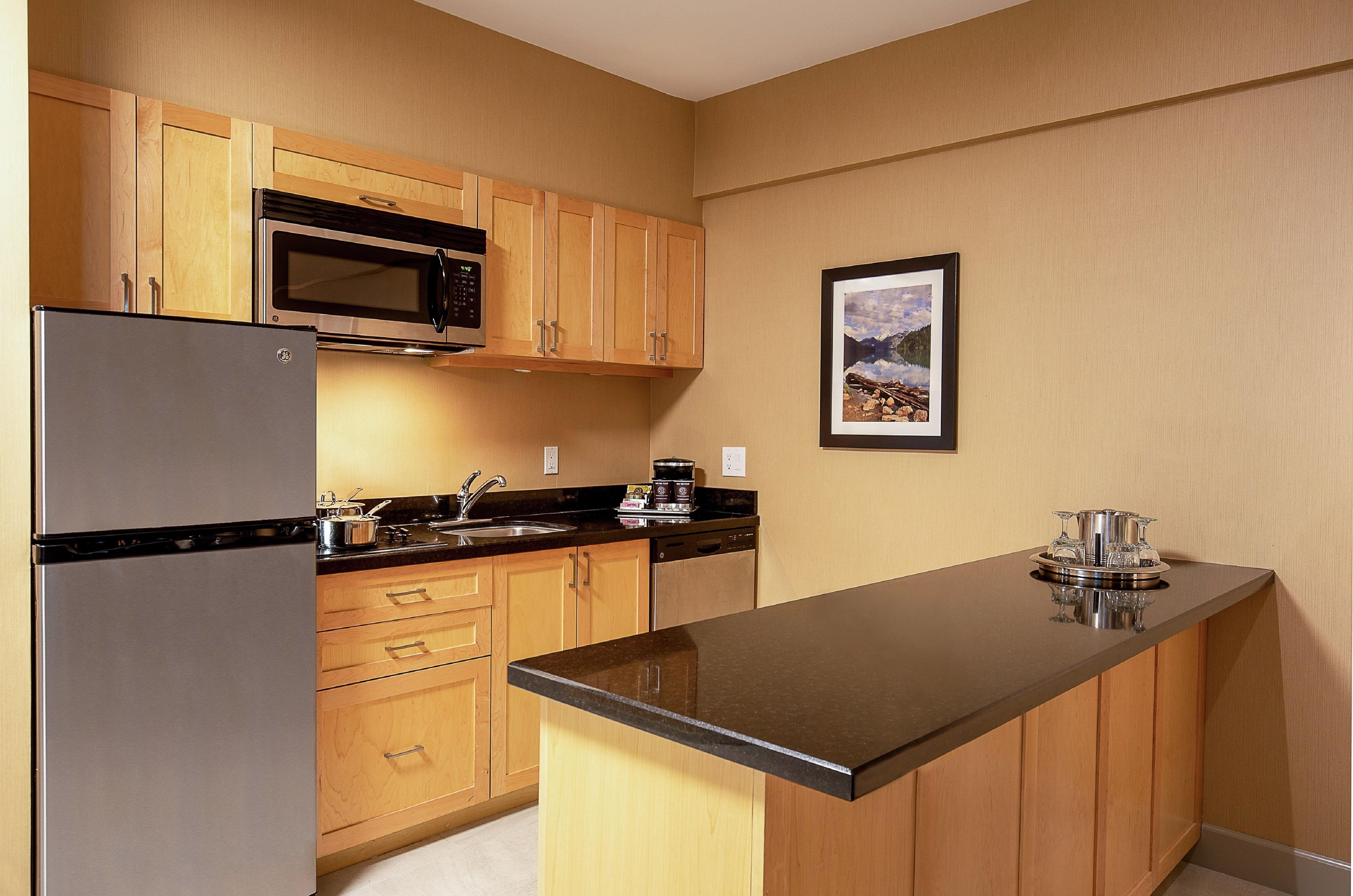 A compact kitchen with wooden cabinets, a stainless steel refrigerator, a microwave, and a coffee maker.