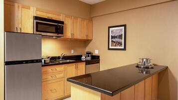 A compact kitchen with wooden cabinets, a stainless steel refrigerator, a microwave, and a coffee maker.