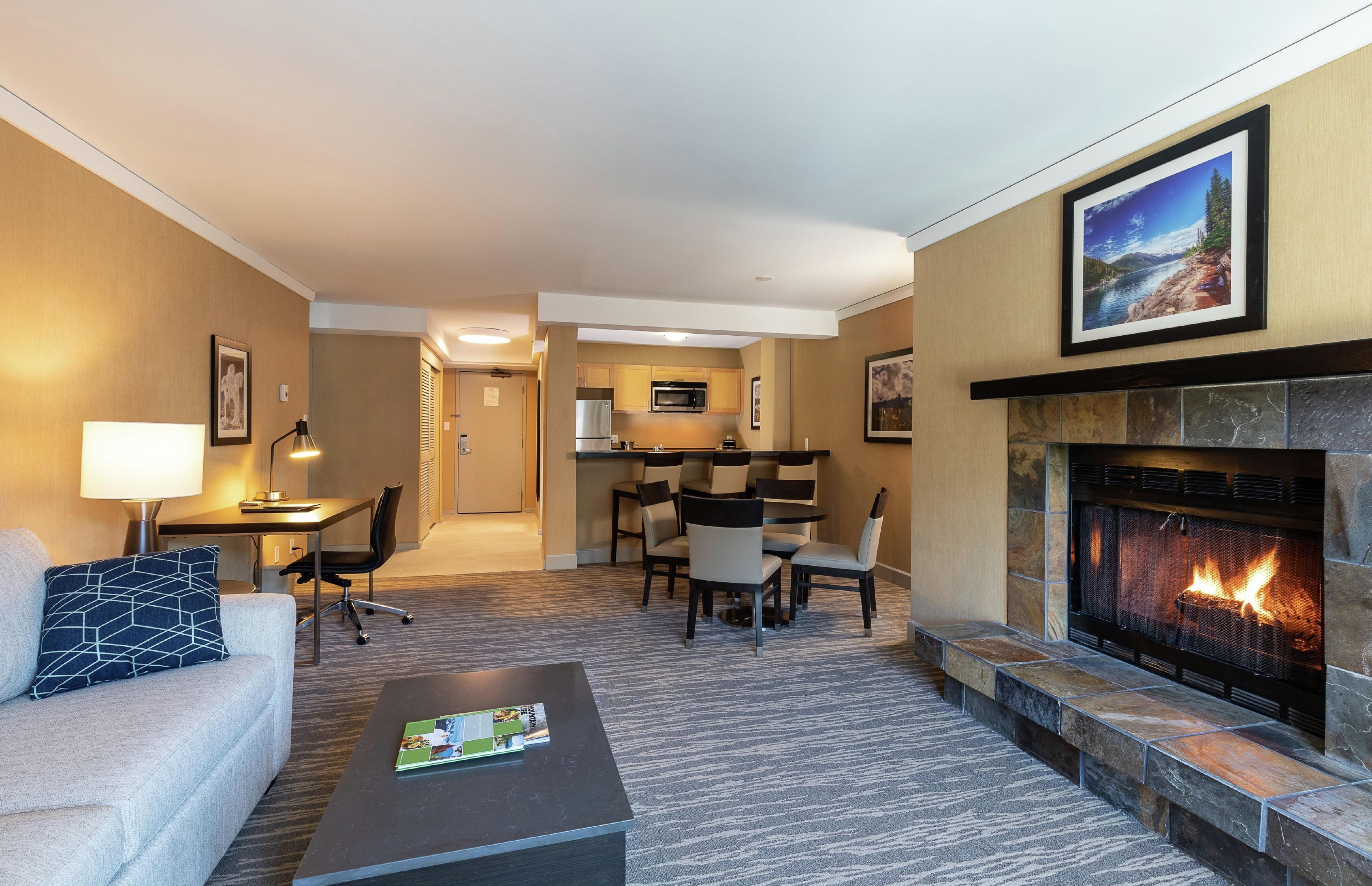 A hotel room with a living area, a fireplace, a dining area, and a kitchen.
