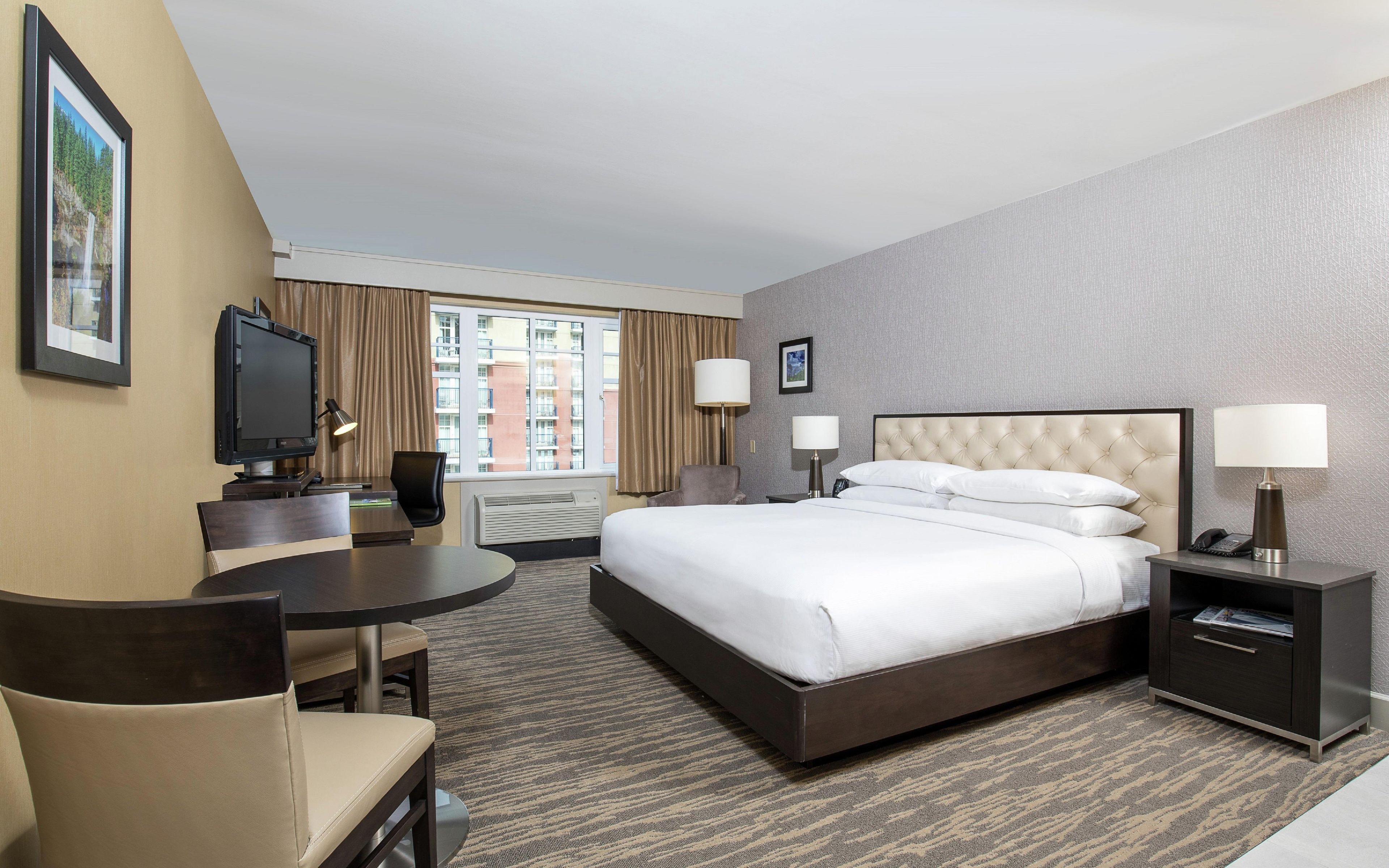 Habitación de hotel con cama, escritorio, silla, televisor y ventana con cortinas.