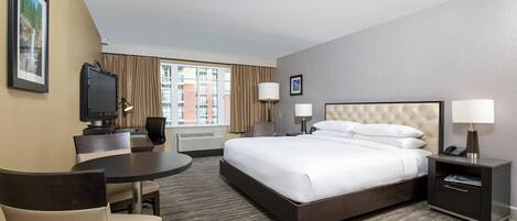 Habitación de hotel con cama, escritorio, silla, televisor y ventana con cortinas.