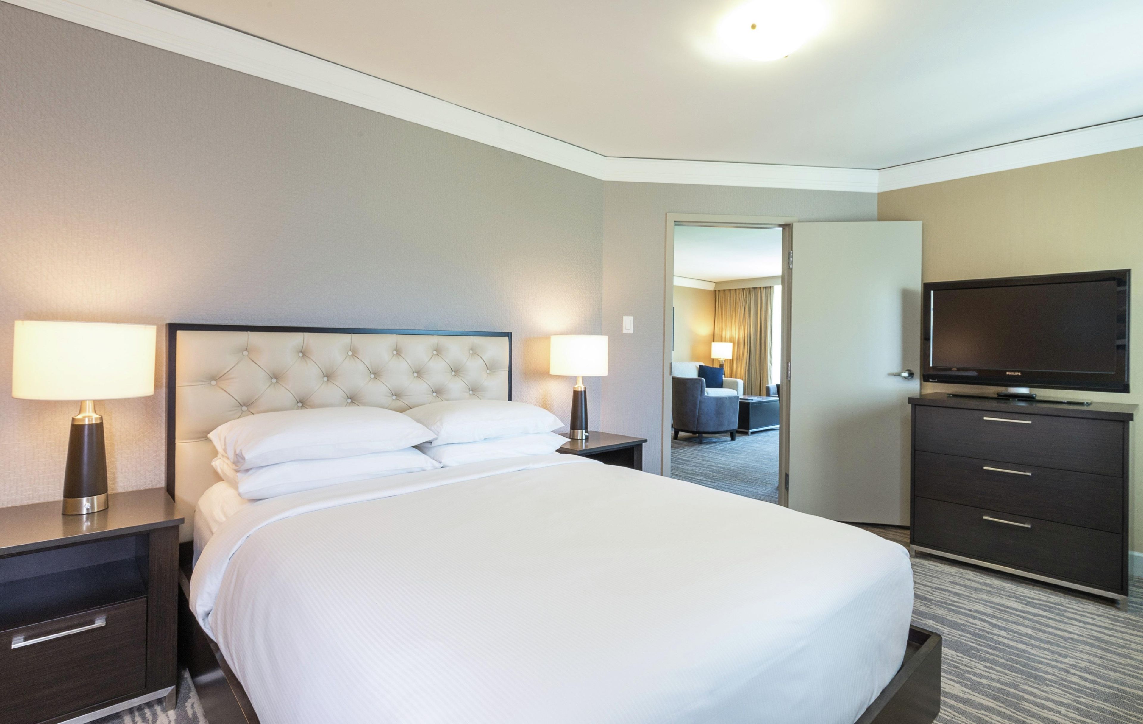 A hotel room with a large bed, two bedside tables with lamps, a television, and a wardrobe.