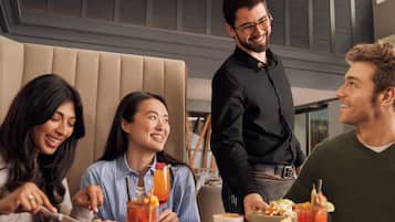 Un grupo de personas cenando en un restaurante, con un camarero sirviendo comida.