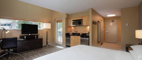 A hotel room with a bed, a desk, a television, a kitchenette, and a bathroom.