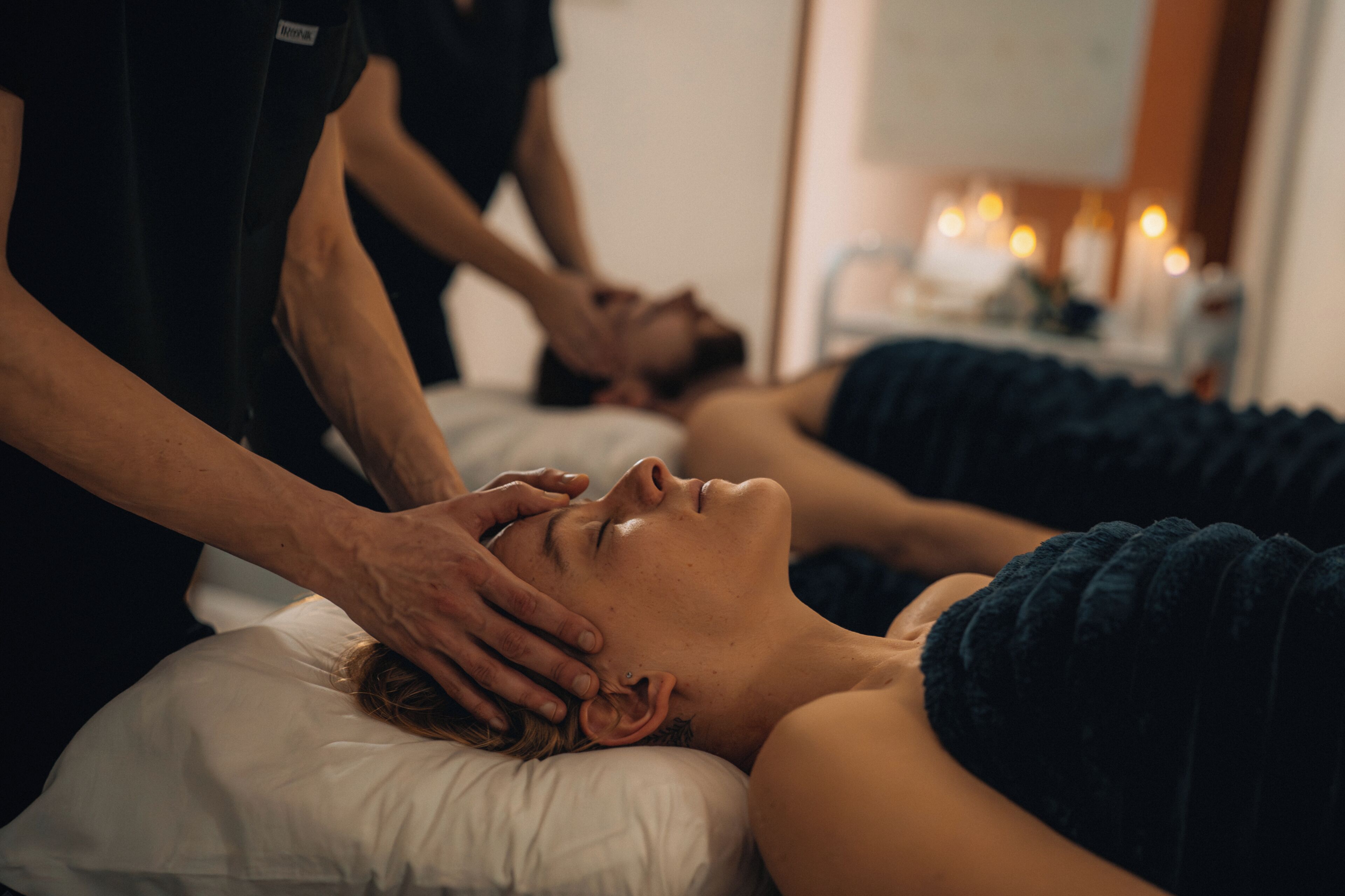 A person receiving a massage in a room with a bed, a white pillow, and a wall-mounted massage table.