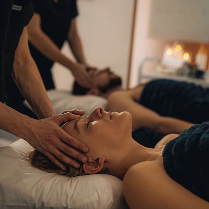 A person receiving a massage in a room with a bed, a white pillow, and a wall-mounted massage table.