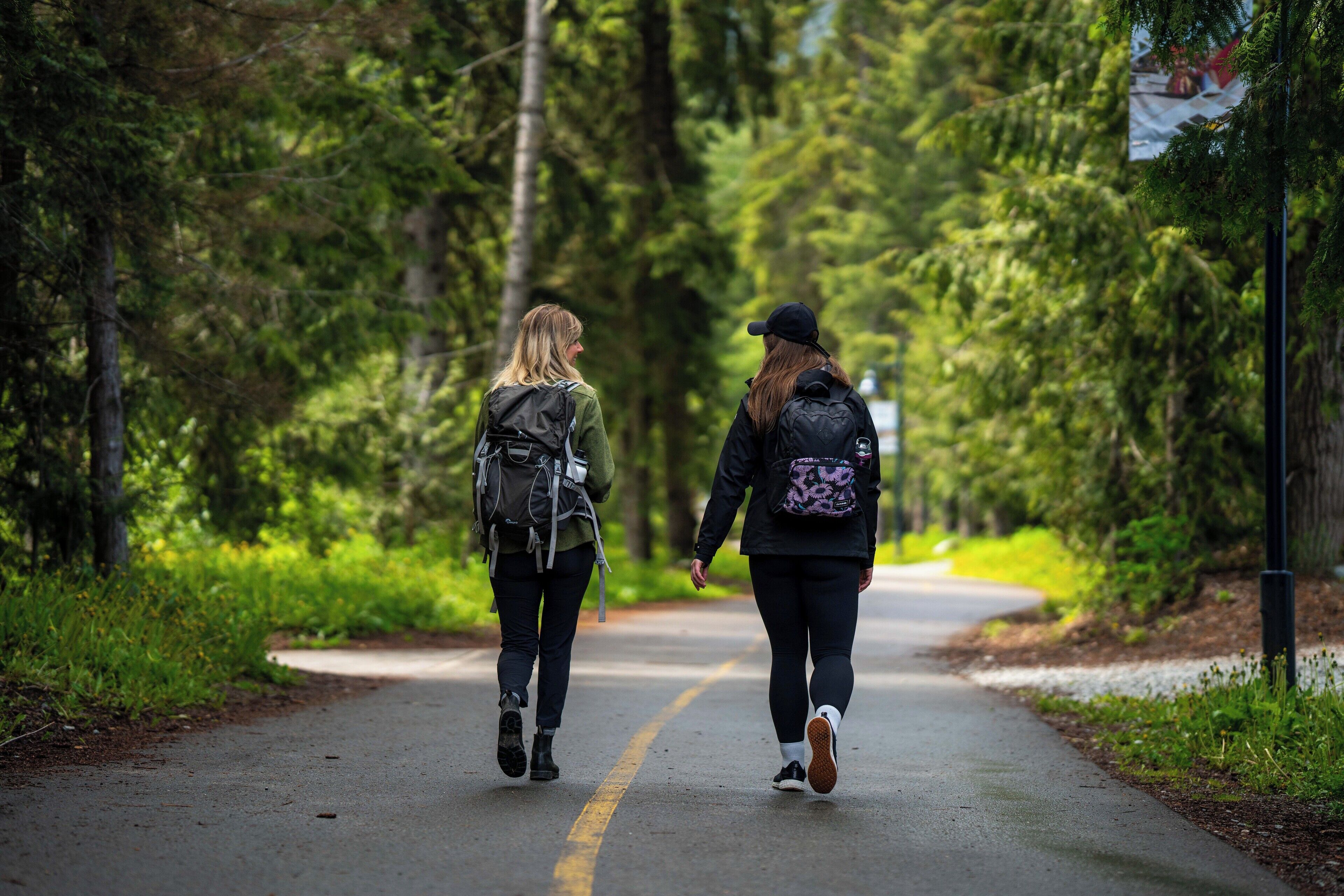 Two people walking on a paved path surrounded by trees.