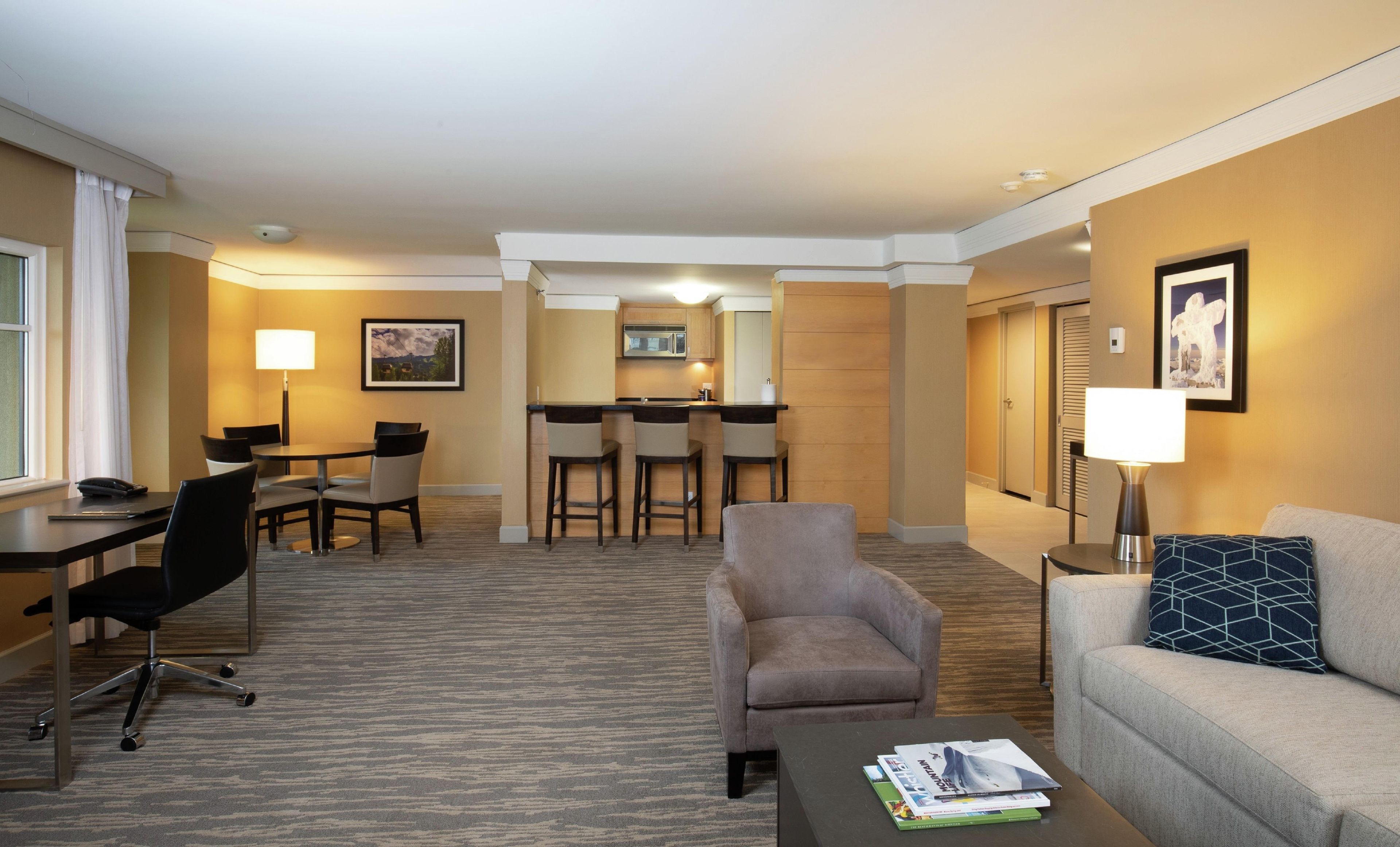 A hotel room with a dining area, a sofa, a coffee table, and a desk with a chair.