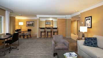 A hotel room with a dining area, a sofa, a coffee table, and a desk with a chair.