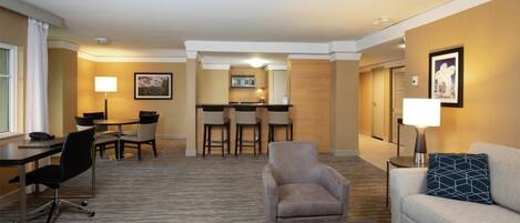 A hotel room with a dining area, a sofa, a coffee table, and a desk with a chair.