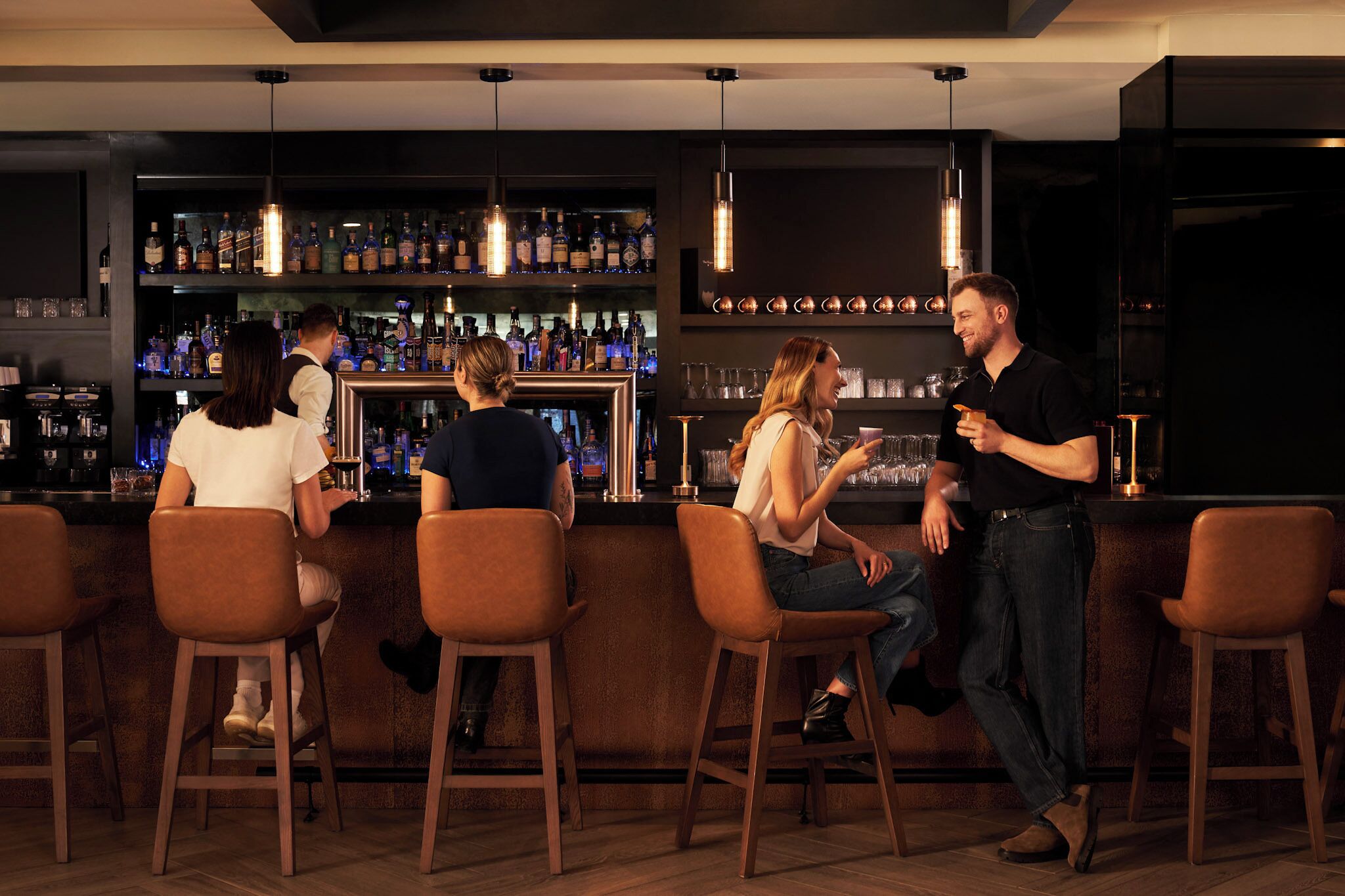 A bar area with multiple stools, a bar counter, and shelves stocked with bottles.