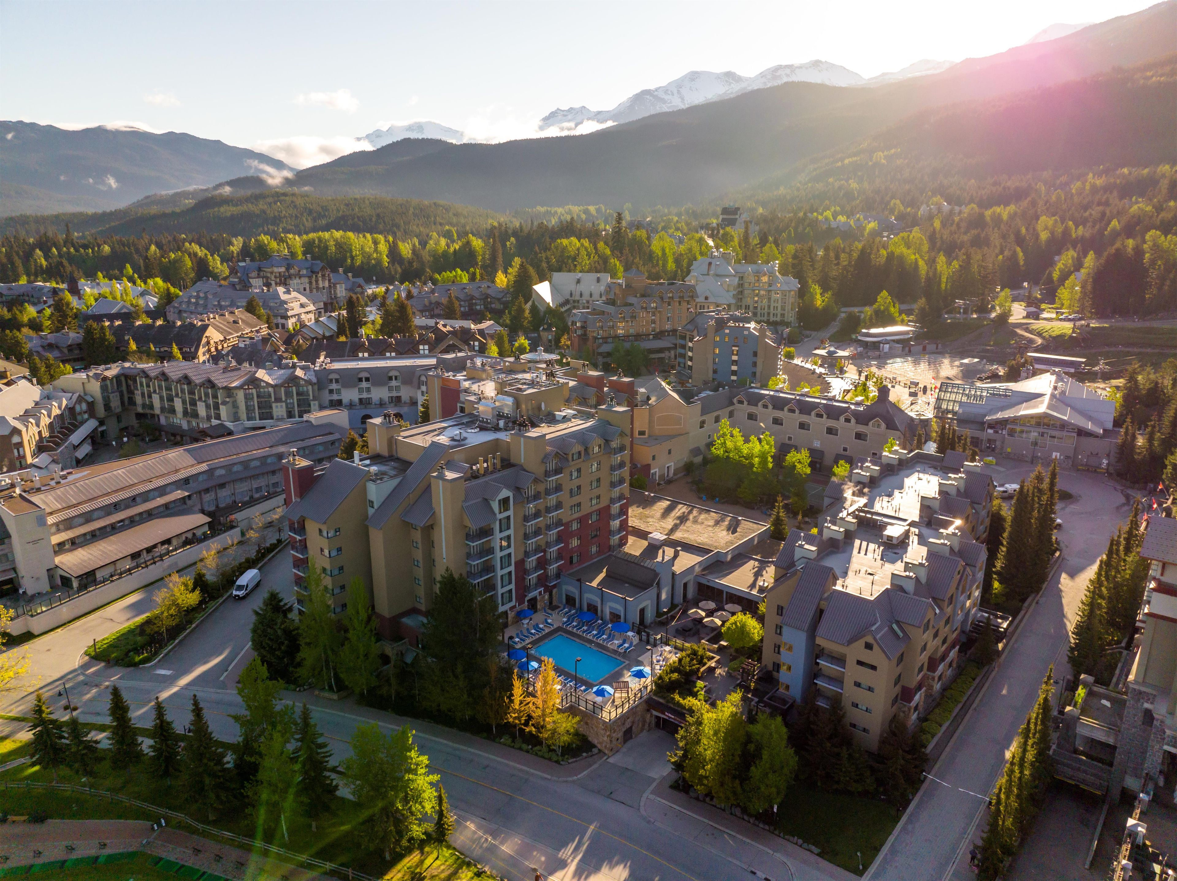 A hotel complex with multiple buildings, a swimming pool, and a parking area.