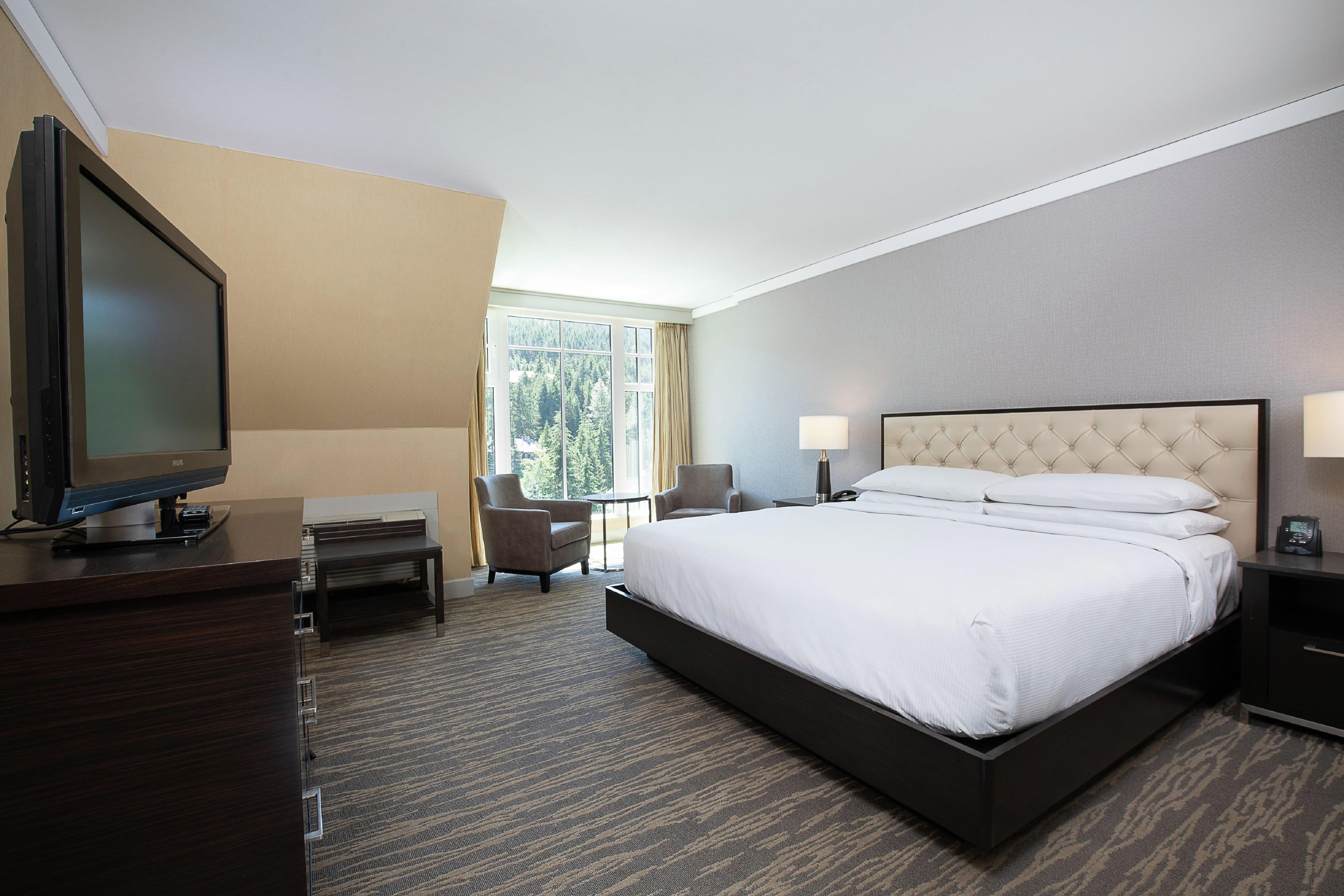 Habitación de hotel con cama, escritorio con televisor, silla y mesita de noche con lámpara.