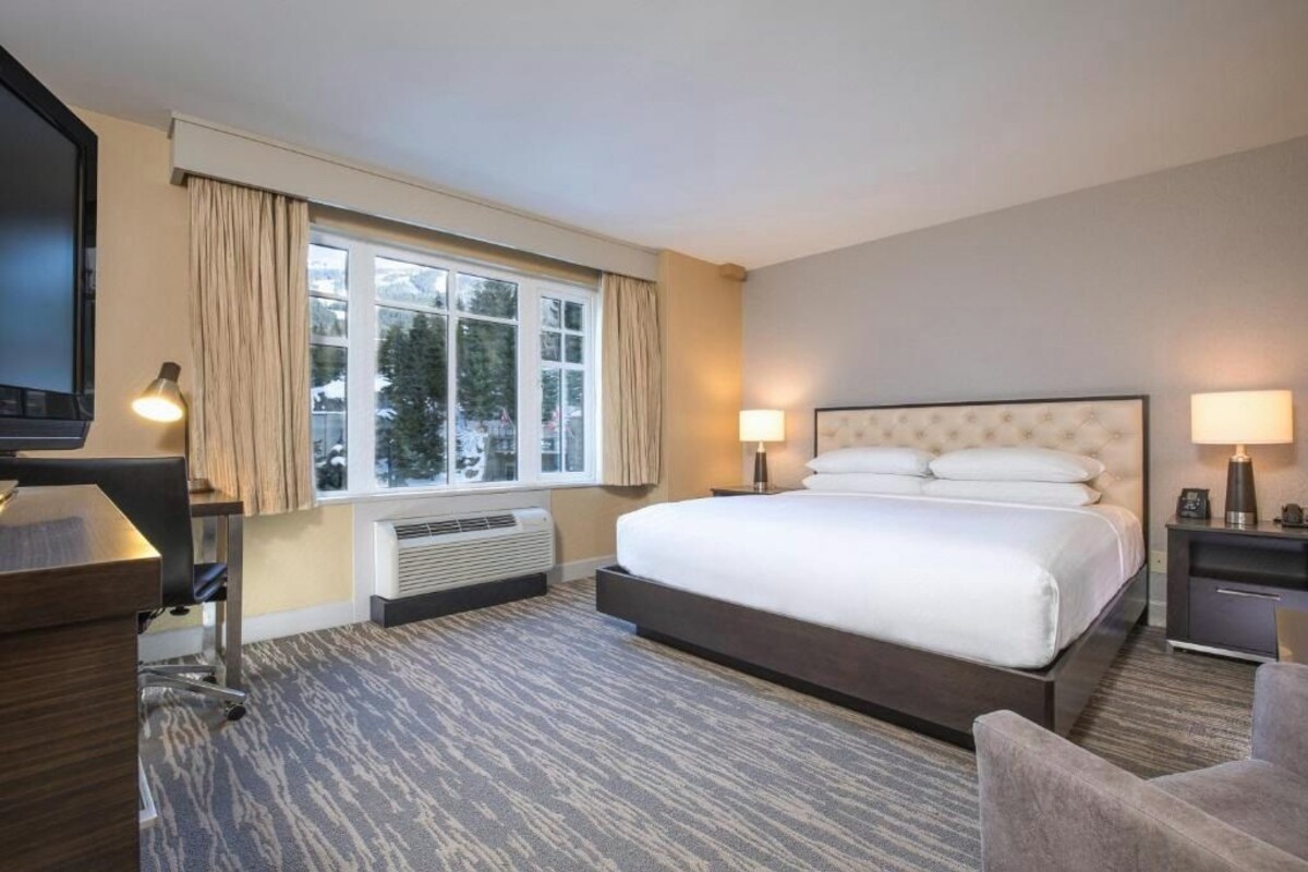A hotel room with a large bed, a desk with a chair, a television, and a window with curtains.