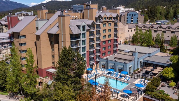 Un hotel con varios pisos, una piscina con tumbonas y vistas a montañas nevadas.
