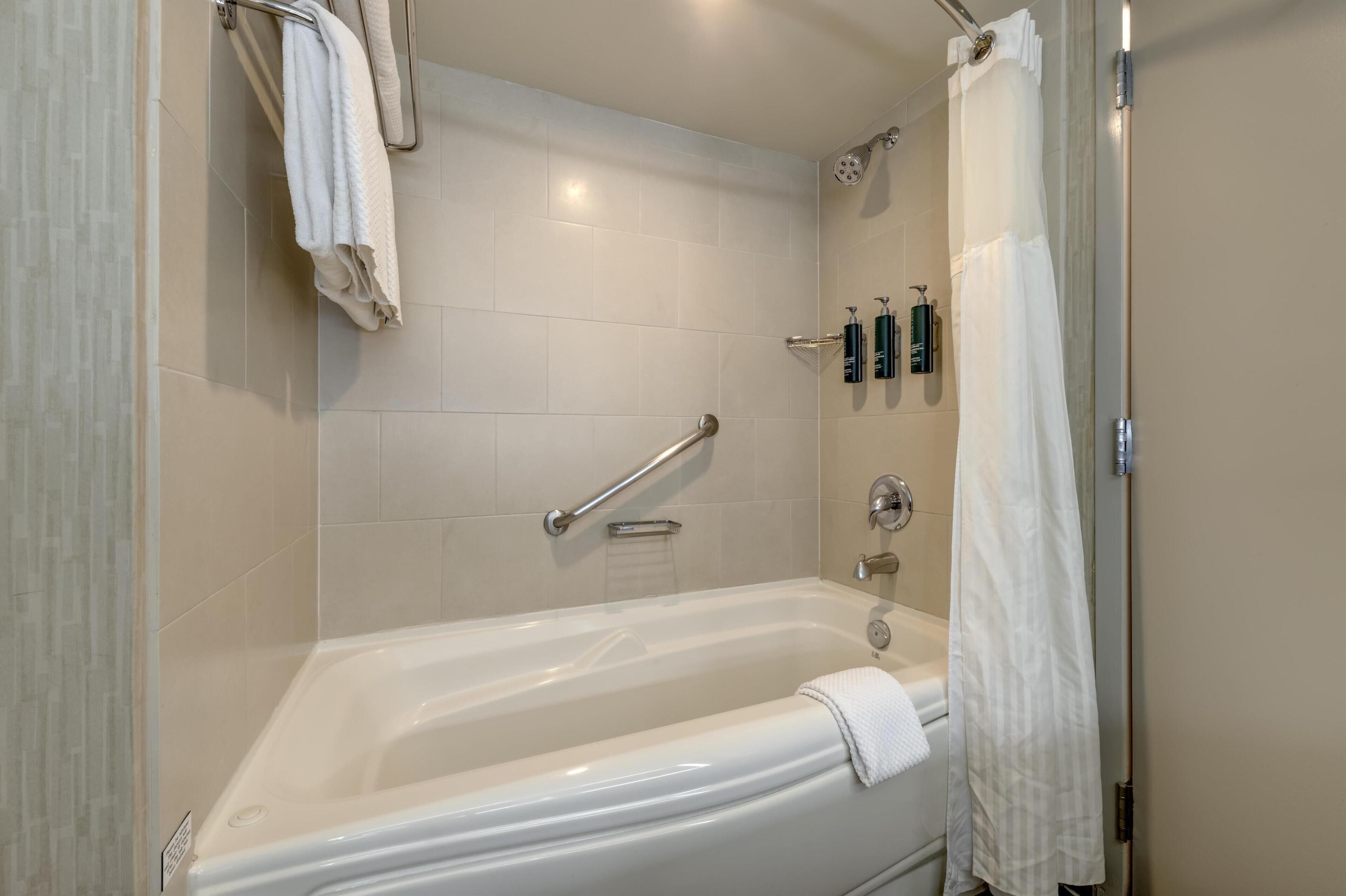 Une salle de bain moderne équipée d’une baignoire, d’un espace douche et d’une barre d’appui.