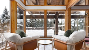 A cozy room with two chairs and a small table, large windows with a view of snow-covered trees and a building outside. - Tantalus Resort Lodge (Whistler)
