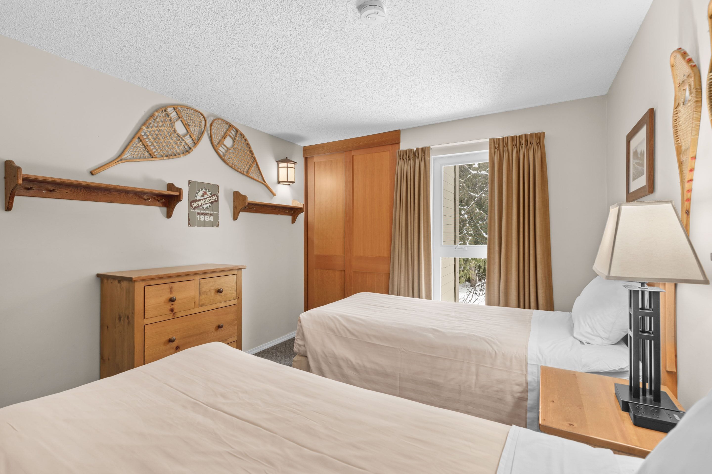 Quarto com duas camas, móveis de madeira, janela com cortinas e decoração na parede.