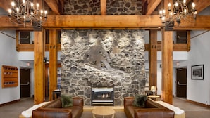 A lobby with a stone wall, wooden beams, leather sofas, a fireplace, and a chandelier. - Tantalus Resort Lodge (Whistler)
