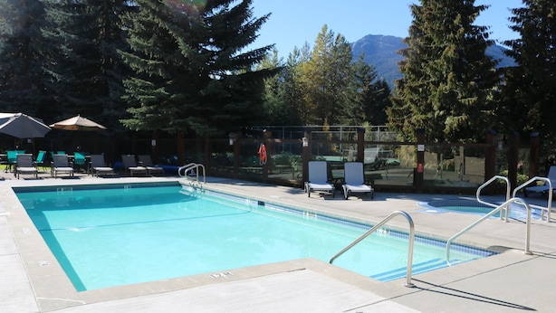 A swimming pool with lounge chairs and umbrellas, surrounded by trees and a mountain view. - Tantalus Resort Lodge (Whistler)