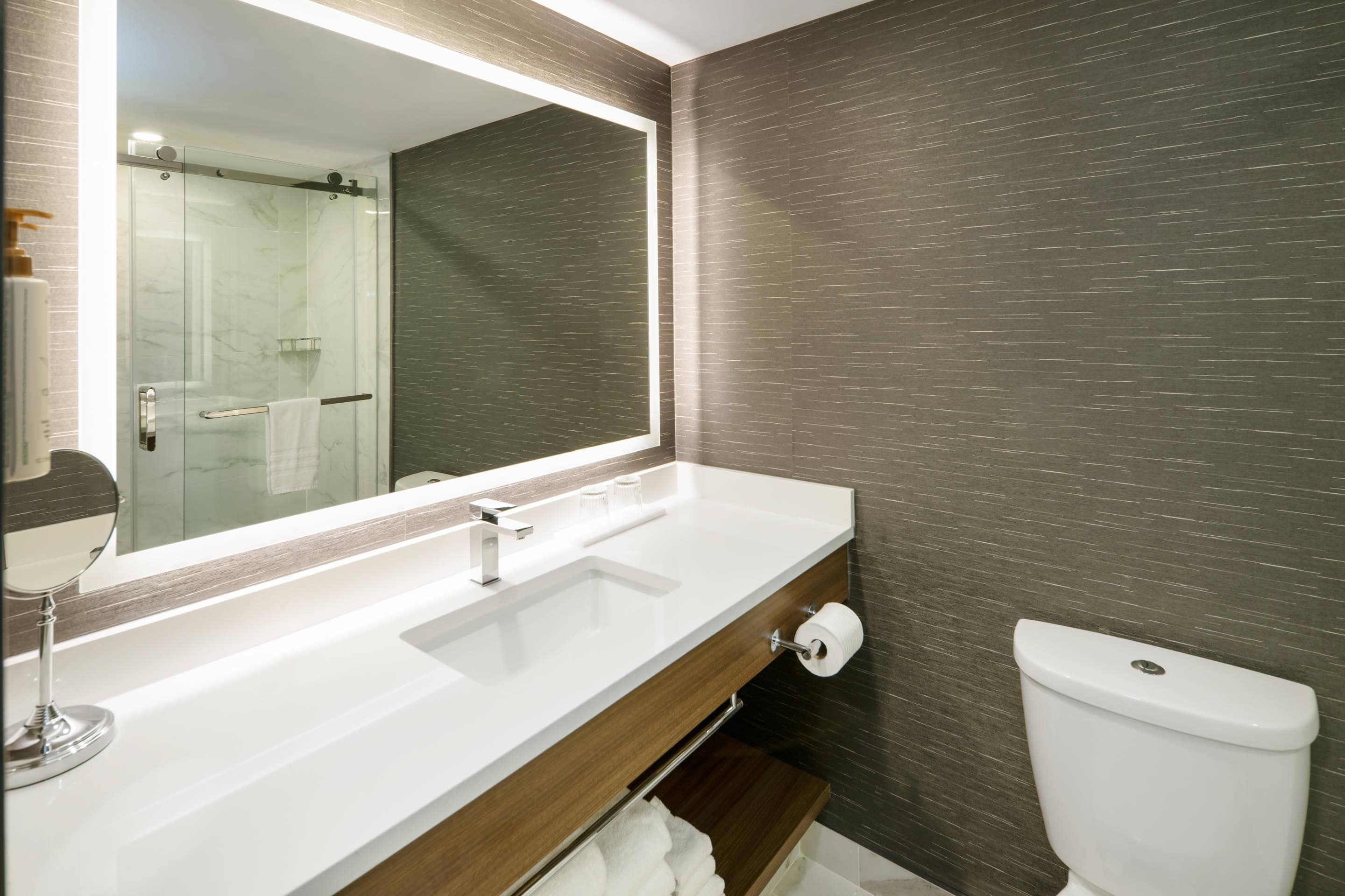 A bathroom with a large mirror, two sinks, a toilet, and a towel rack.