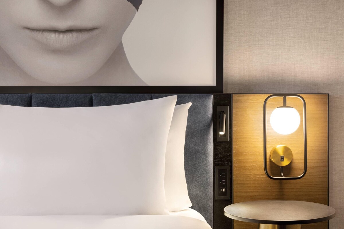 Una habitación de hotel con cama, una mesa redonda y una lámpara fijada a la pared.
