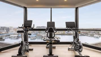 Un gimnasio con tres bicicletas estáticas, ventanas amplias y vistas al puerto deportivo.