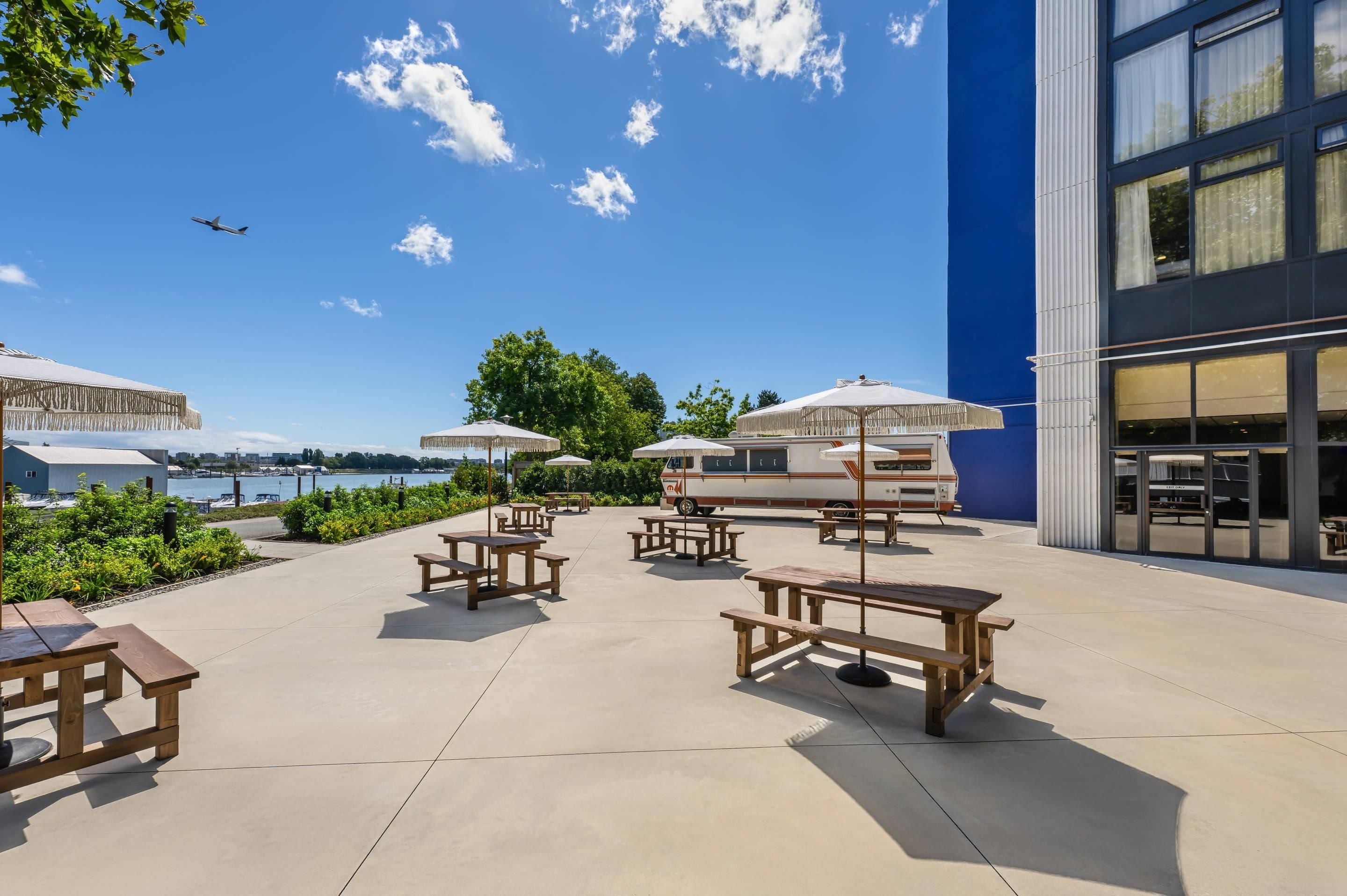 An outdoor patio with picnic tables and umbrellas, overlooking a body of water and a marina.