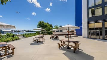 An outdoor patio with picnic tables and umbrellas, overlooking a body of water and a marina.