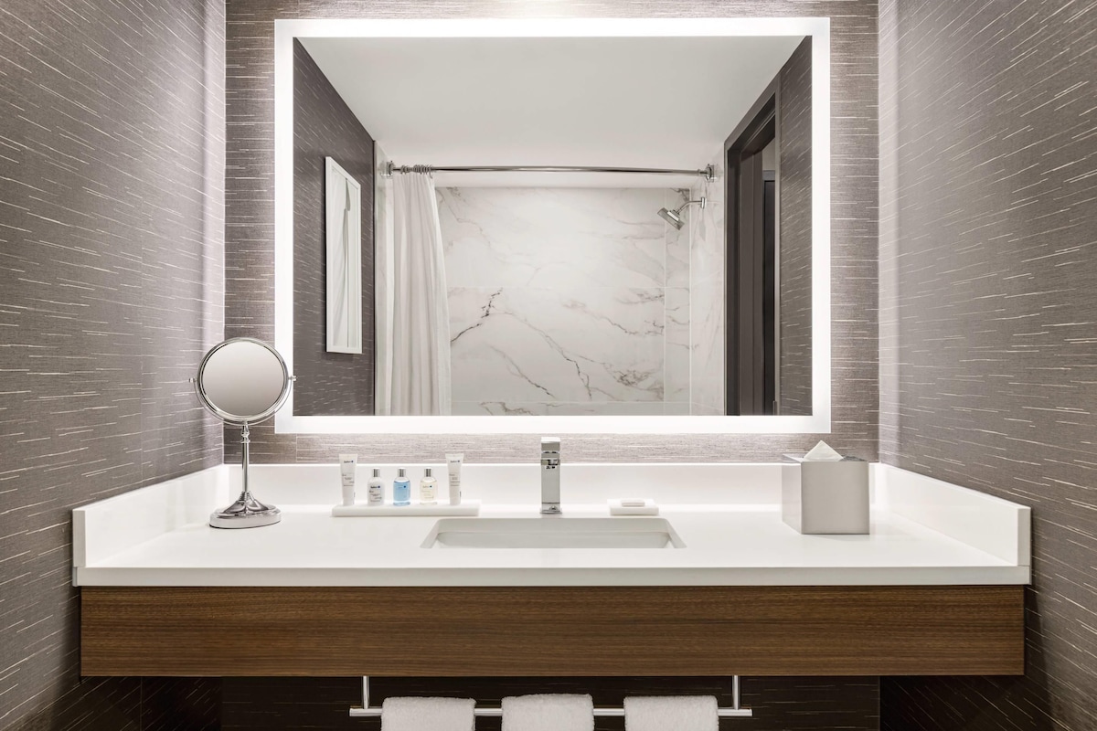 A modern bathroom with a marble vanity, a large mirror, and a shower with a curtain.