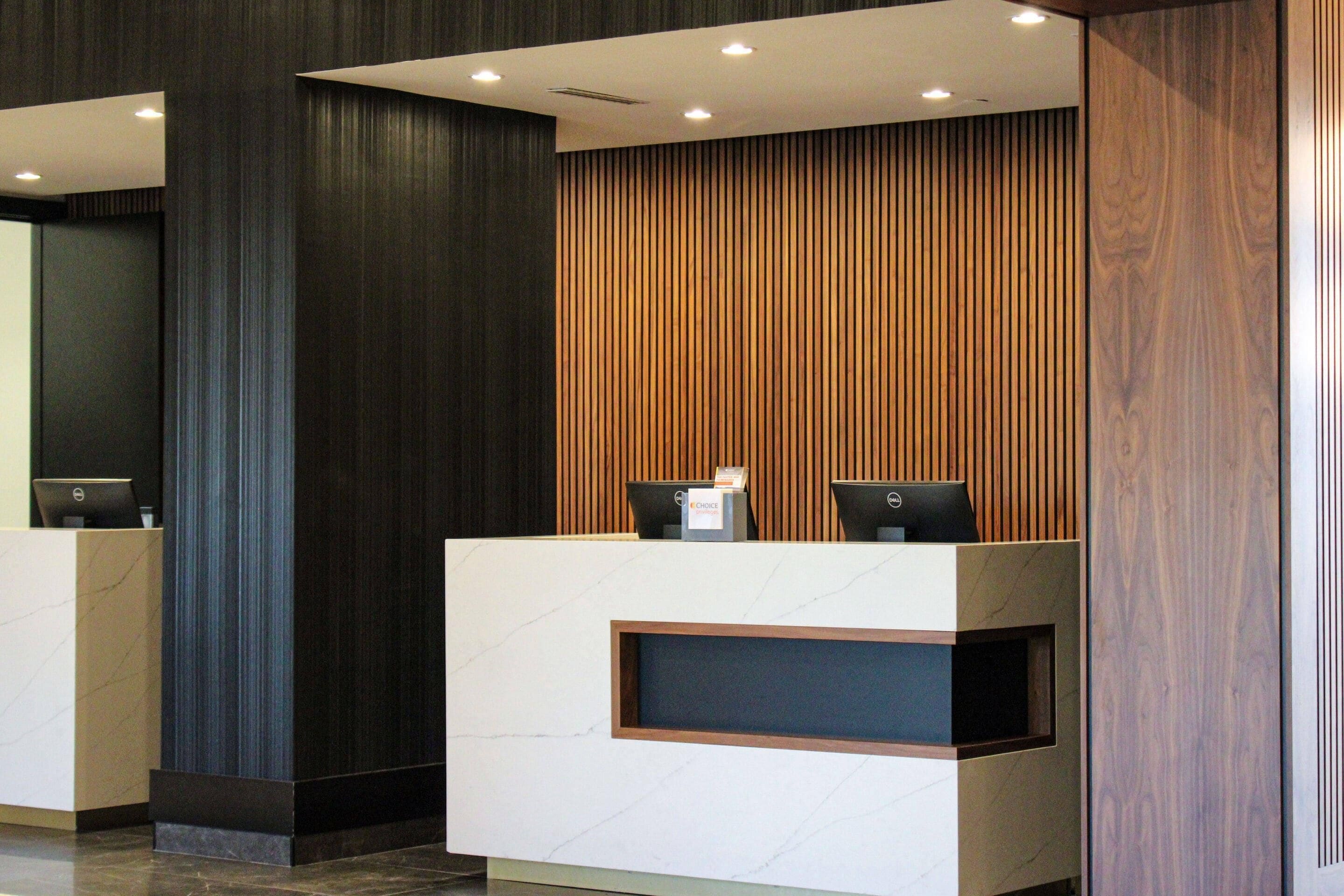 A reception desk with two computer monitors, a digital screen, and a wooden panel wall.