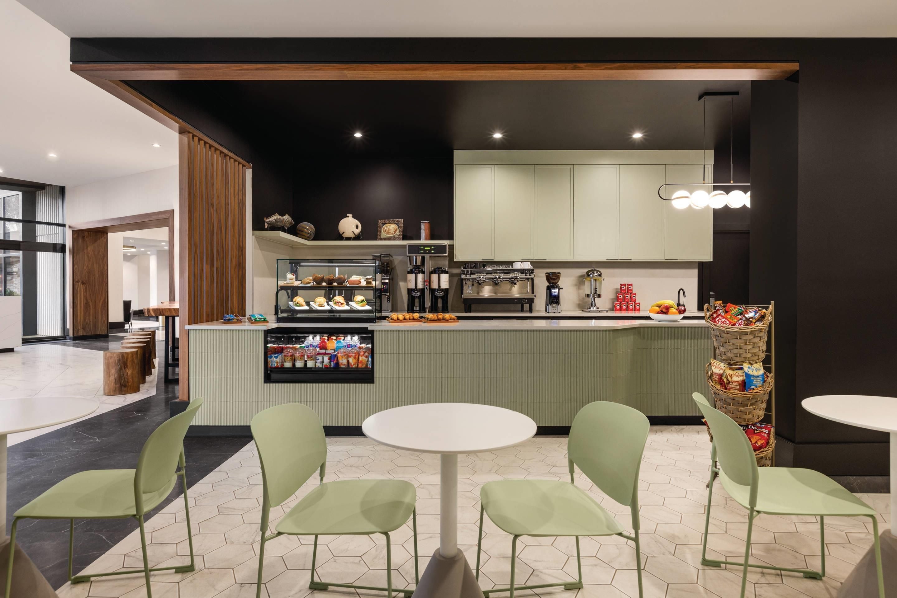 Un café moderno con mostrador central, zona de estar y cocina al fondo.