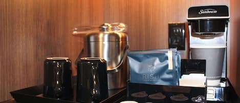 A coffee station with a Sunbeam coffee maker, a stainless steel coffee pot, and a tray with tea and coffee pods.