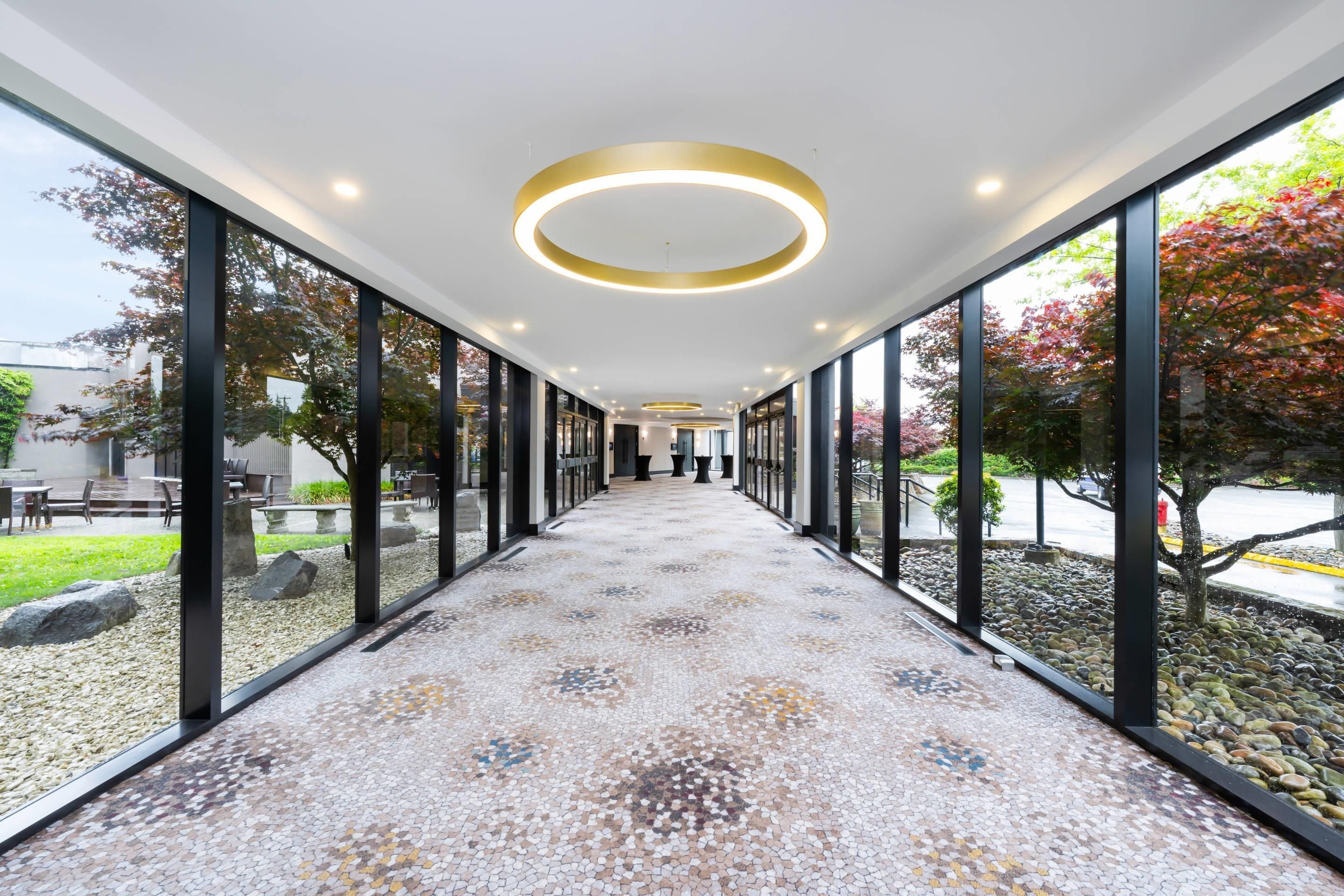 Un pasillo con suelo estampado, ventanas amplias y luces de techo circulares.